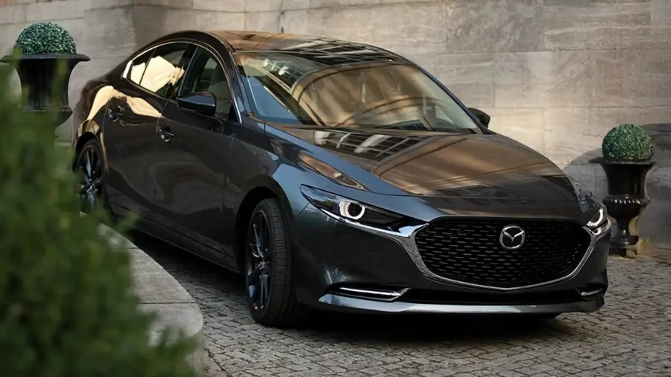 Mazda 3 sedán oscuro estacionado en un camino de adoquines 